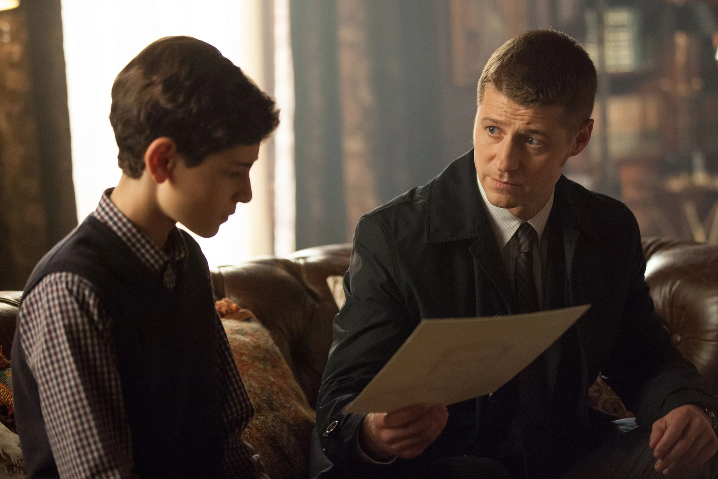 Un Bruce Wayne aún niño, a la izquierda, observa una foto que le muestra un adulto Jim Gordon, a la derecha
