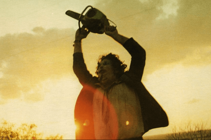 Un hombre ataviado con traje y una máscara de piel humana, Leatherface, alza triunfante una motosierra